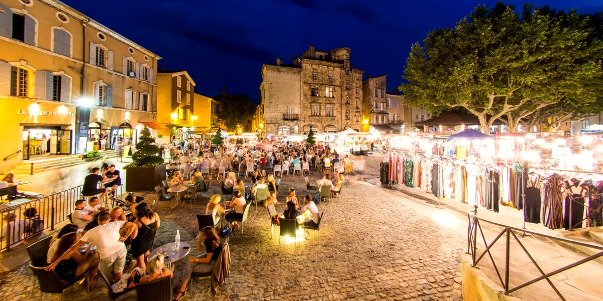 Long trestle tables at a rural French night market, strung with lights